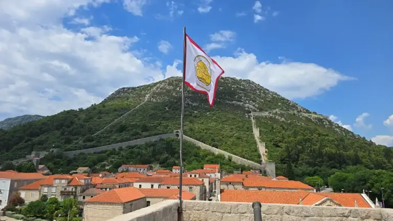 Ston Flag flying over the rooftops of Ston, with the wall winding up the hill to the fortress Wall