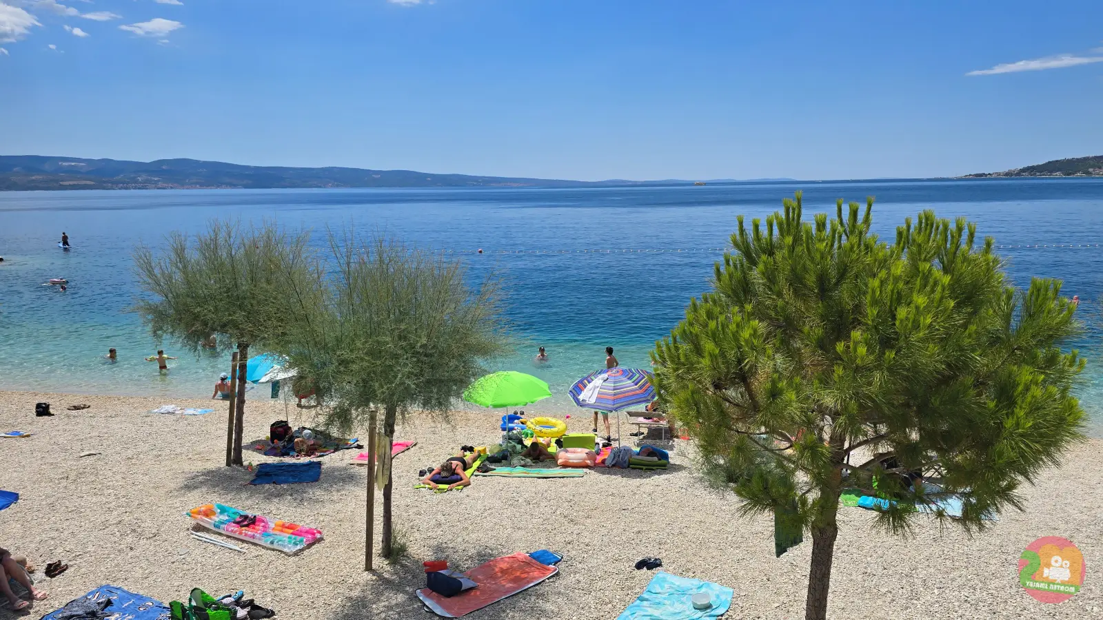 Brzet pebble beach in Omiš with pine trees, swimmers and clear turquoise water