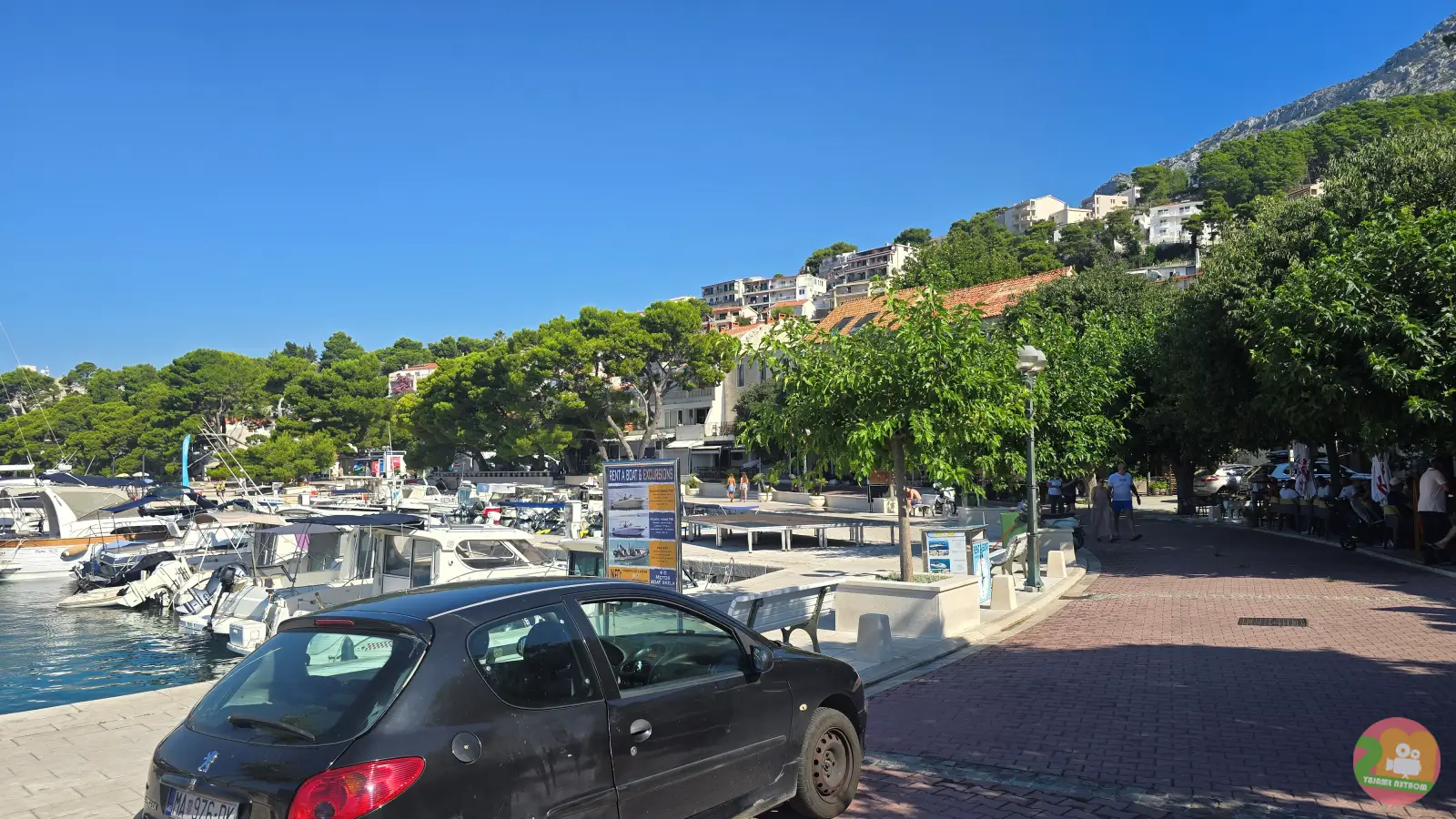 Riva u centru Brele s privezanim brodicama, stablima i kućama na padini
