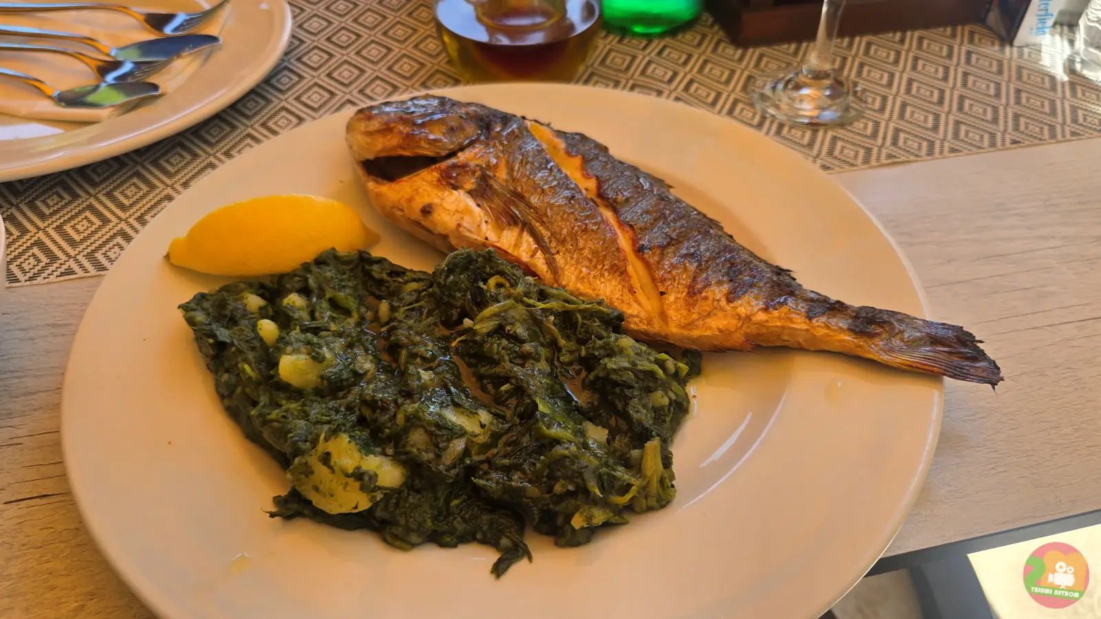 Grilled sea bream with Swiss chard, potatoes and a lemon wedge on a white plate