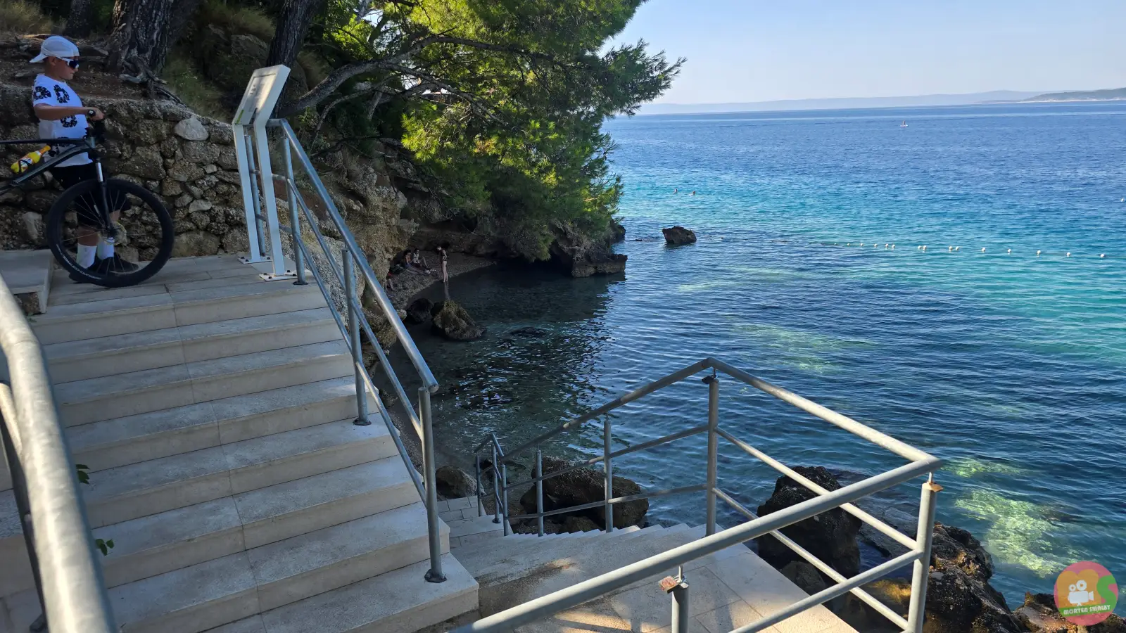 Steintreppe mit Metallgeländer an der Promenade von Brela über den Felsen der Höhle Medvidina, unten klares Meer