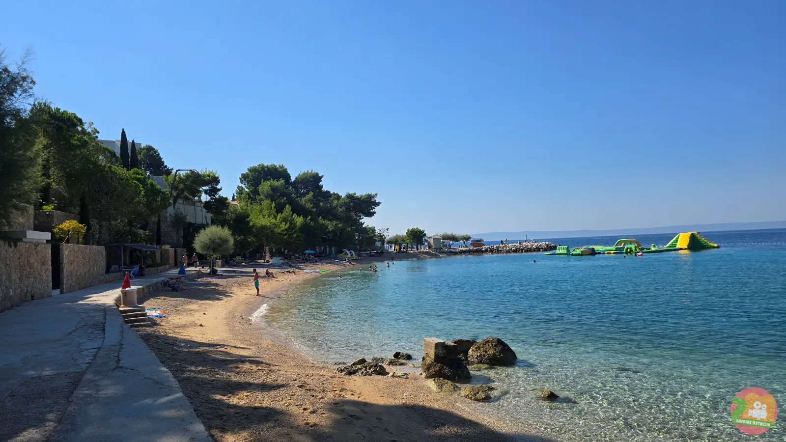 Zakrivljena plaža sa sitnim šljunkom u Breli i plutajućim vodenim parkom na moru