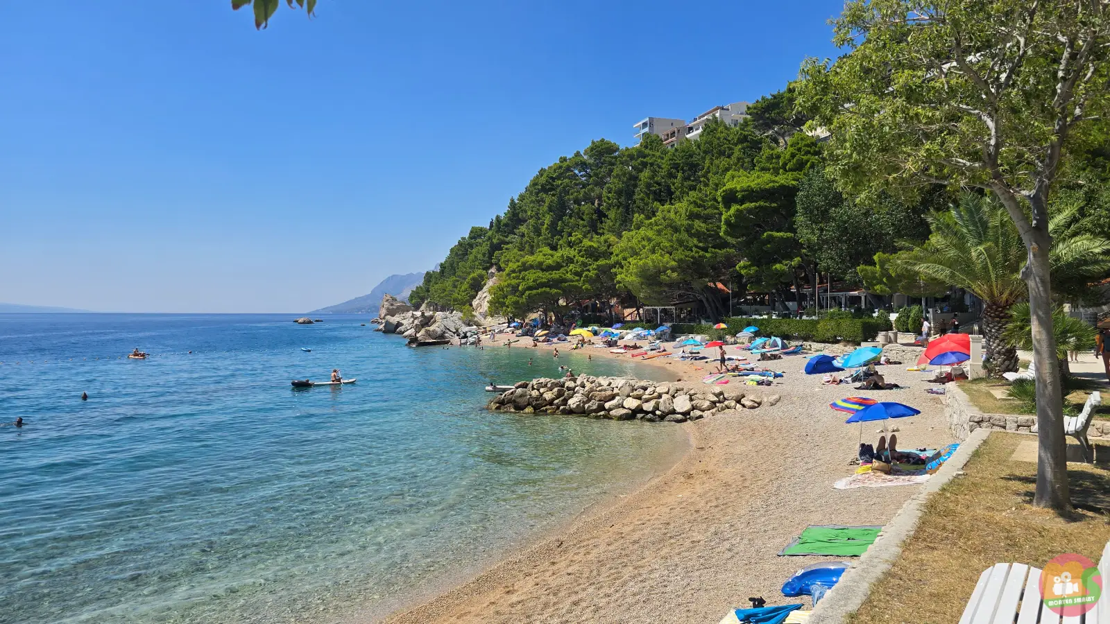 Podcrkavlje Beach in Brela, a curved pebble beach with colourful parasols, a stone breakwater and pine-covered slopes