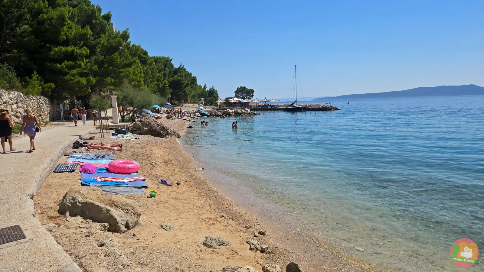 Uska plaža uz šetnicu u Breli s ručnicima, mirnim morem i otokom Bračem na obzoru