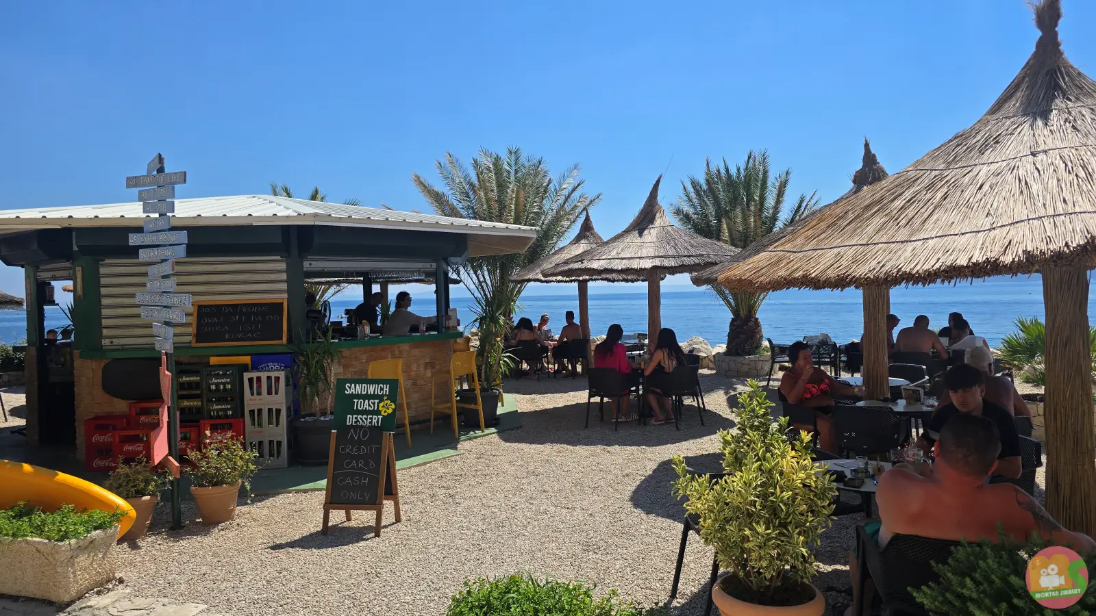 Strandbaren Waikiki i Brela med stråparasoller, palmer og gæster ved bordene ved havet