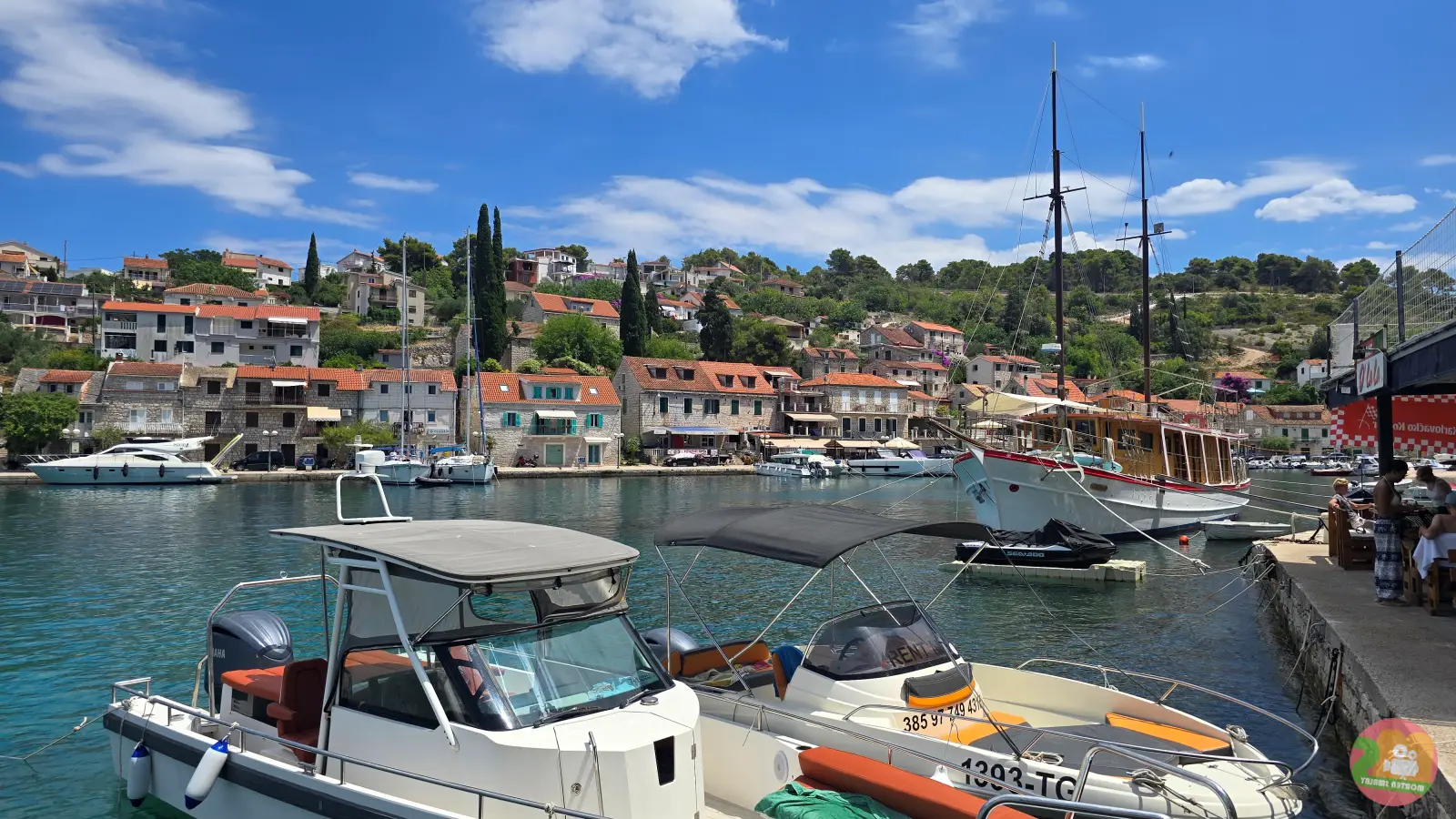 Hafen von Stomorska auf Šolta mit hölzernem Segelschiff, Motorbooten und Häusern mit roten Dächern am Hang