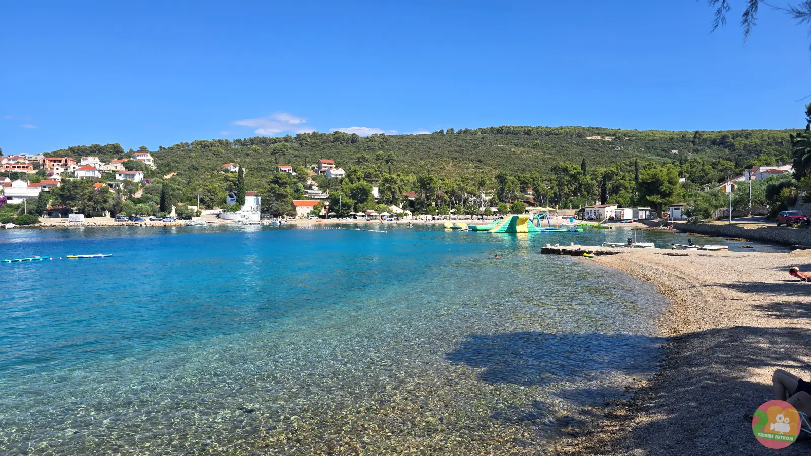 Żwirowa plaża w Nečujamie na Šolcie z płytką turkusową wodą i dmuchanym parkiem wodnym