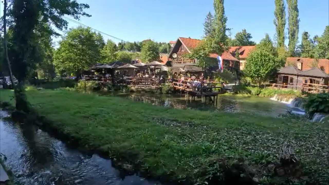 Restaurantterrasser bygget ud over floden mellem træhuse og grønne plæner i Rastoke
