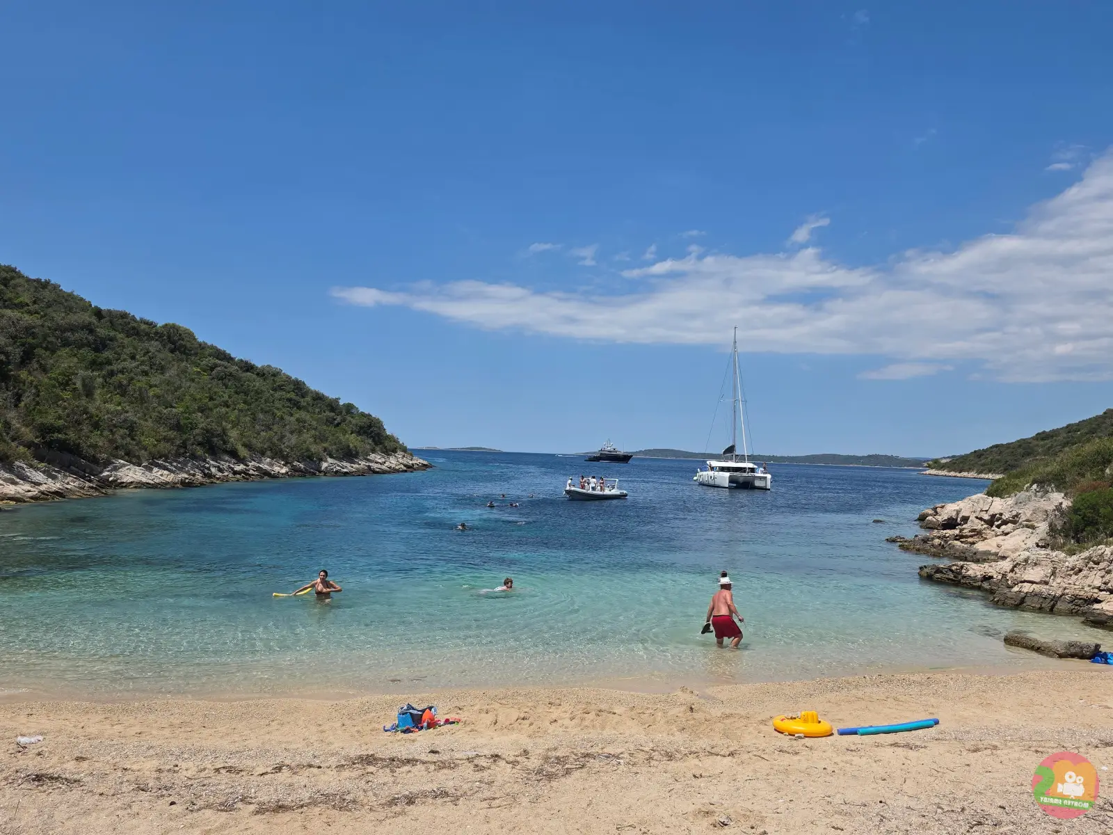 Sandstrand in der Bucht Šipova auf Šolta mit Badenden, Katamaran und klarem flachem Wasser zwischen grünen Hügeln